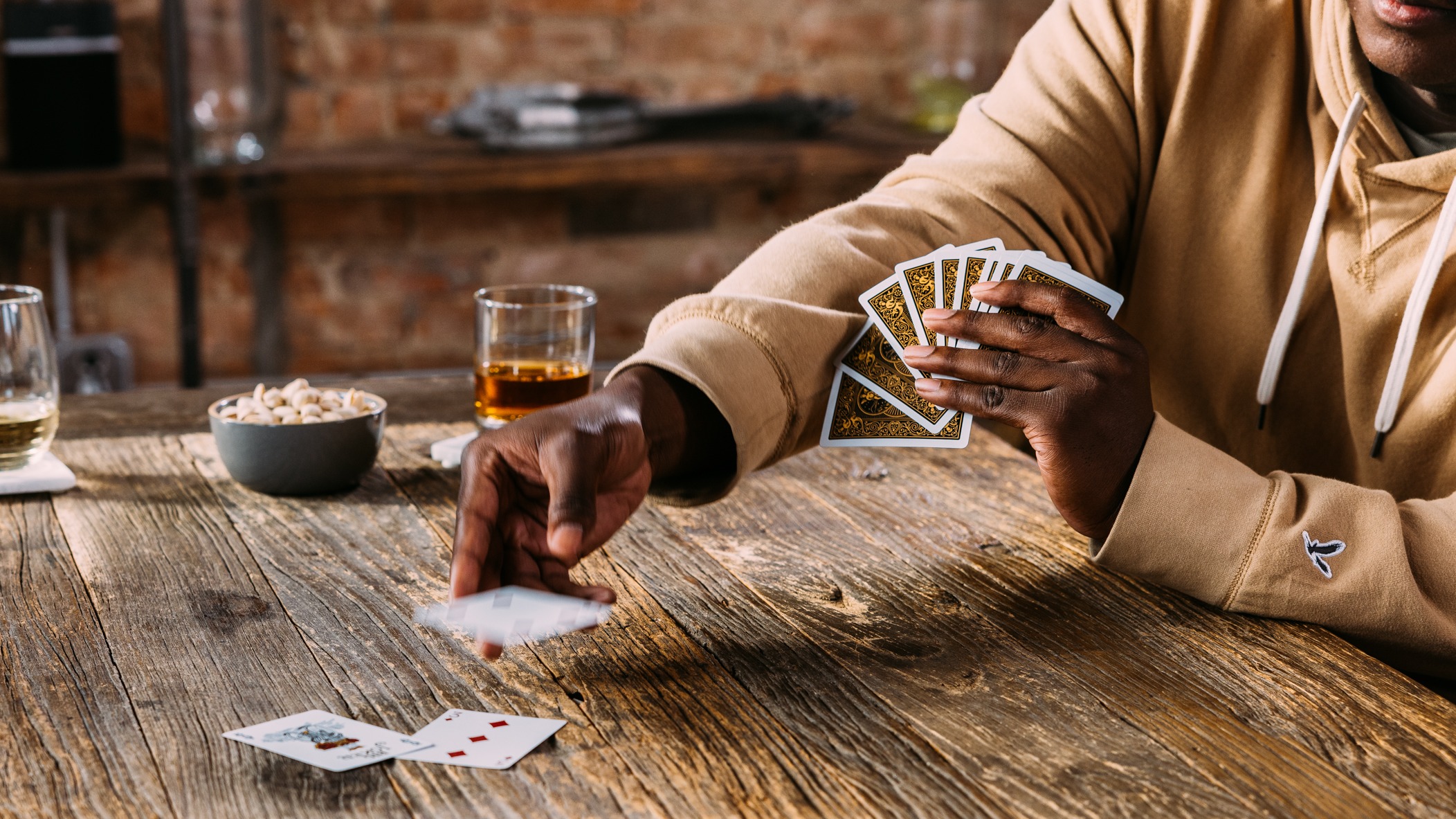 Person throwing down card into play pile on wooden table, with drinks and snacks around.
